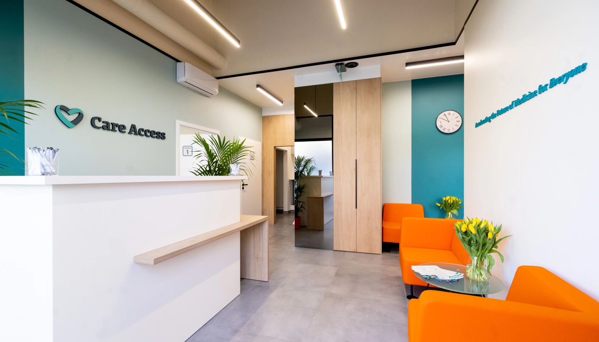 Nowoczesna i jasno oświetlona recepcja kliniki medycznej Care Access z recepcją, pomarańczowymi siedziskami, zielonymi roślinami i oznakowaniem ściennym